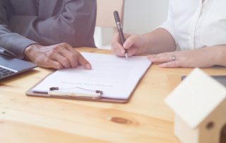 A woman signing a contract with a wooden model house on the desk