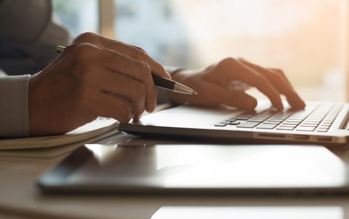 Someone taking notes while looking at a computer.