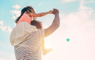 A father with his young daughter sitting on his shoulders.