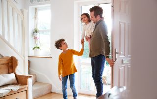 A man and two children walking through the front door of their home.