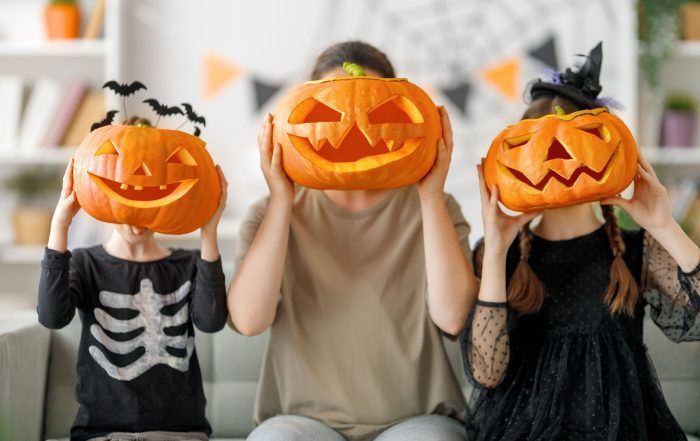 A mother and two children holding up carved pumpkins to their faces.