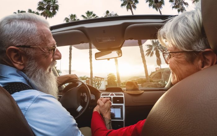 A happy older couple driving in a convertible car.