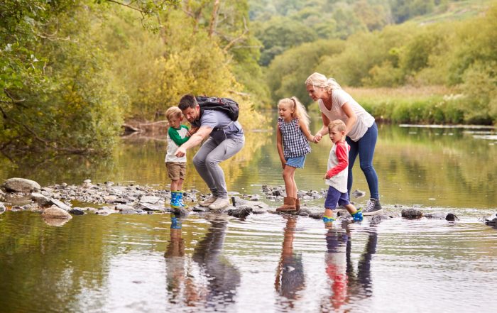 A family with young children crossing a river while hiking.
