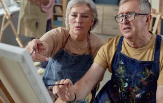 An older couple painting at an easel together.