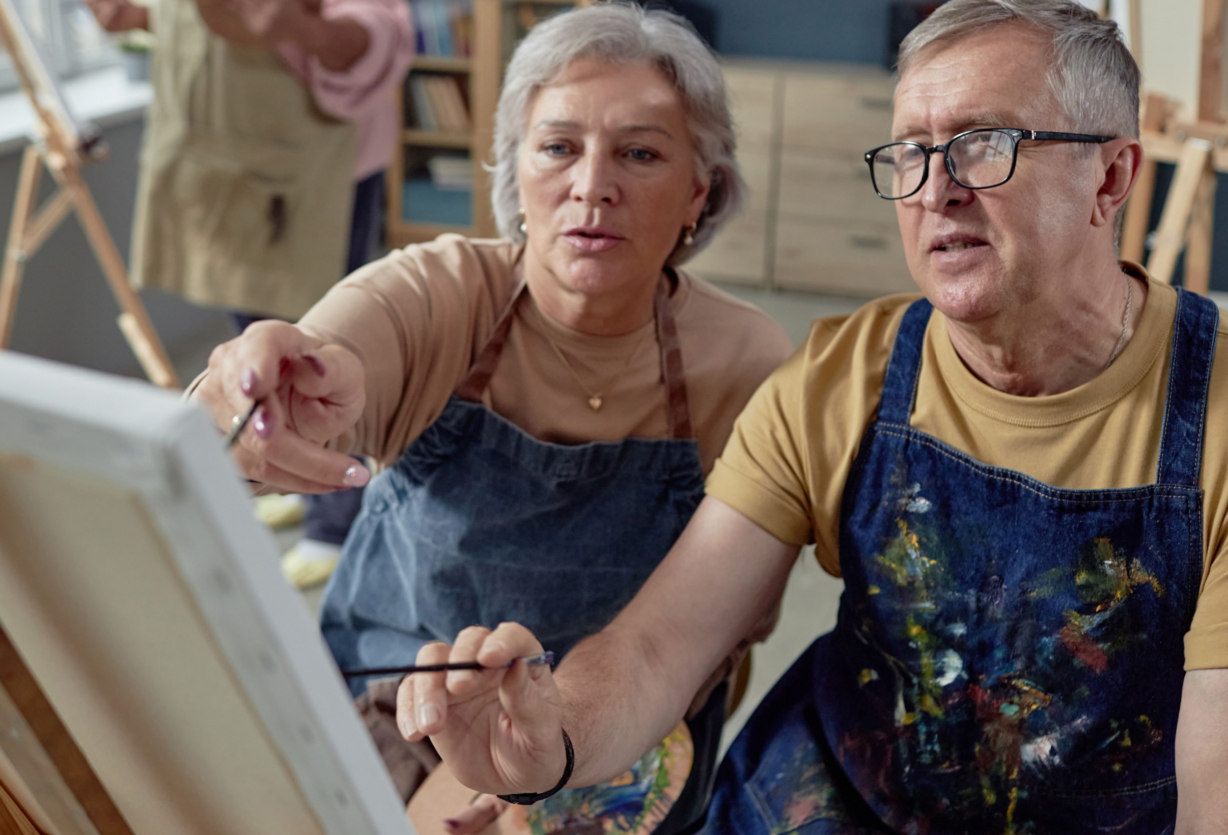 An older couple painting at an easel together.