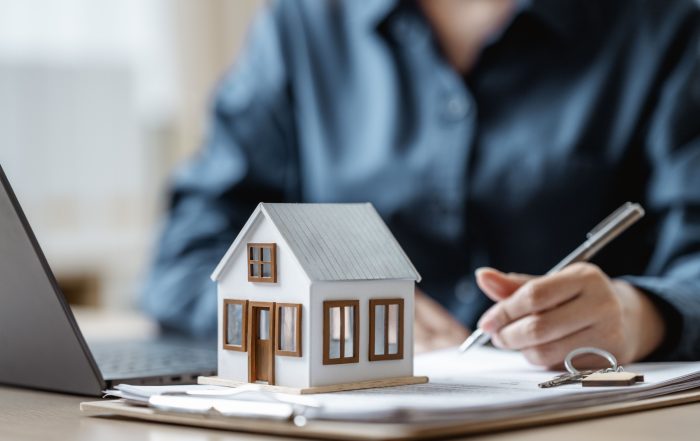 A person signing a document with a model house on the table.