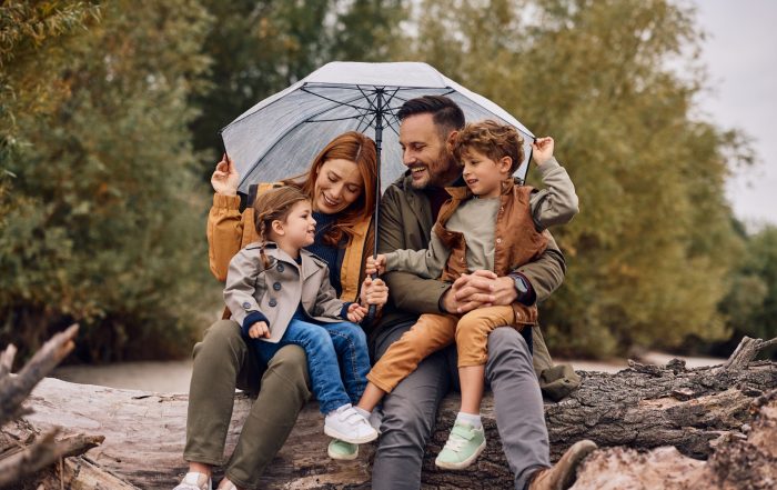 A young family sheltering under an umbrella and smiling